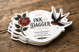 Stack of custom die-cut 24pt recycled uncoated business cards for Ink and Dagger featuring gold foil stamped accents and traditional tattoo artwork
