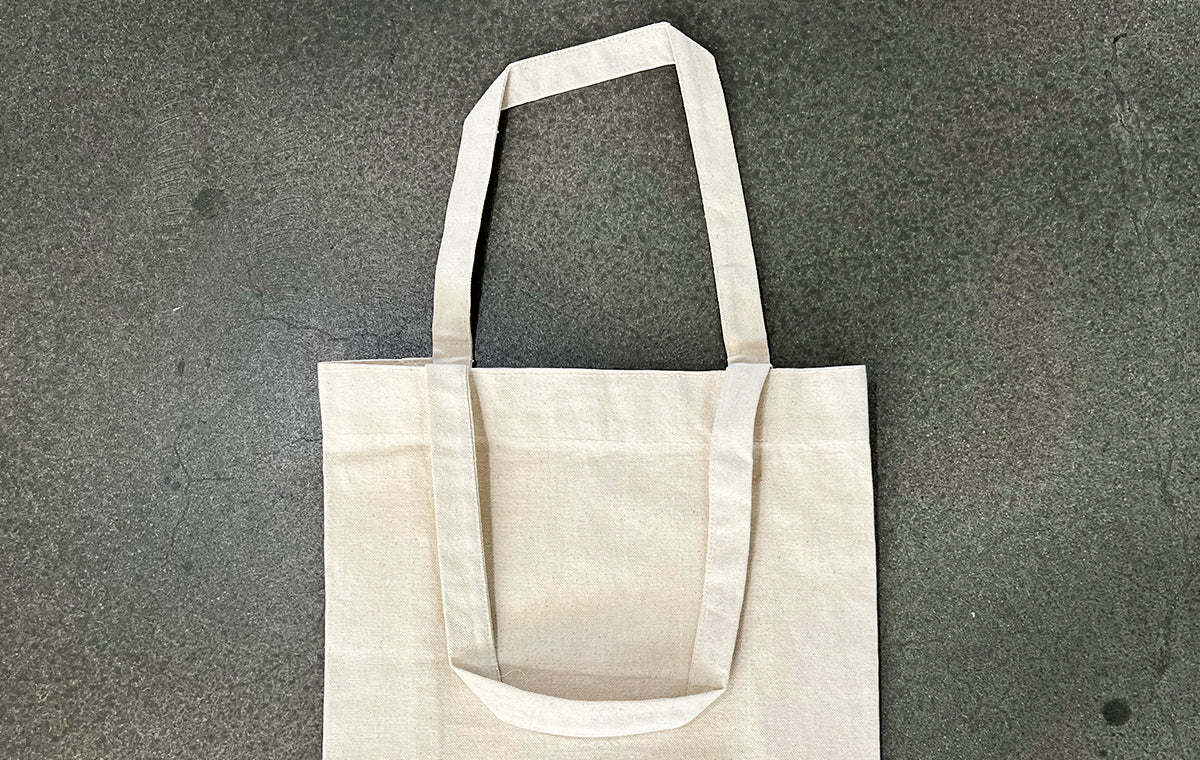 Blank natural cotton tote bag with gusset resting flat on a grey concrete surface
