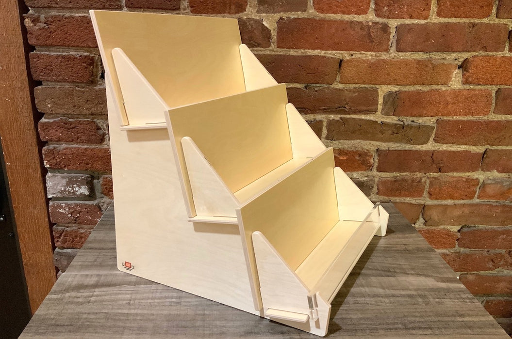 Side of a 3-tier birch plywood retail card stand made in USA with acrylic front in front of a brick wall.