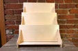3-tier birch plywood retail card stand made in USA with acrylic front in front of a brick wall.