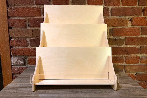 3-tier birch plywood retail card stand made in USA with acrylic front in front of a brick wall.