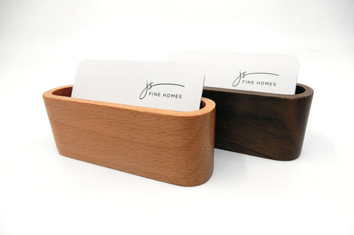 Light stain wood business card stand in front of a dark stain wood business card stand both holding horizontal JS Fine Homes silk laminated business cards.