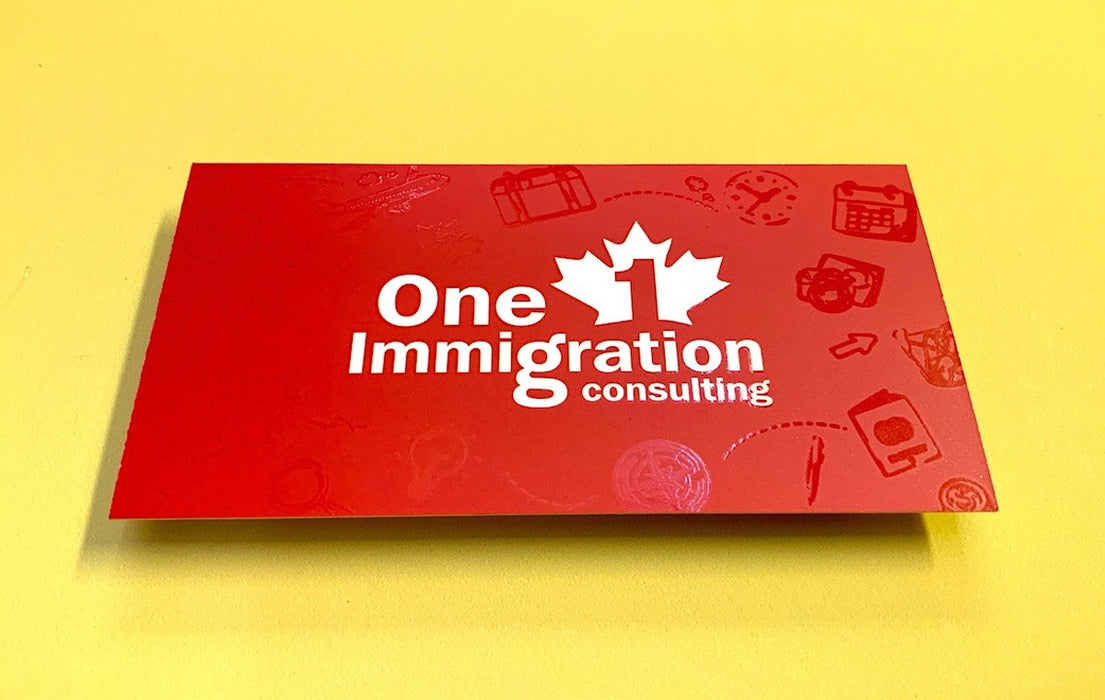Business cards for One Immigration Consulting on silk laminated 19pt stock | Red background with their logo in the middle | There are travel items like suitcase, passport, and camera around the logo in spot gloss | Clubcard Printing USA